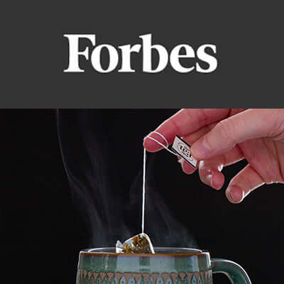 a hand pullsa tea sachet out of a steaming ceramic mug