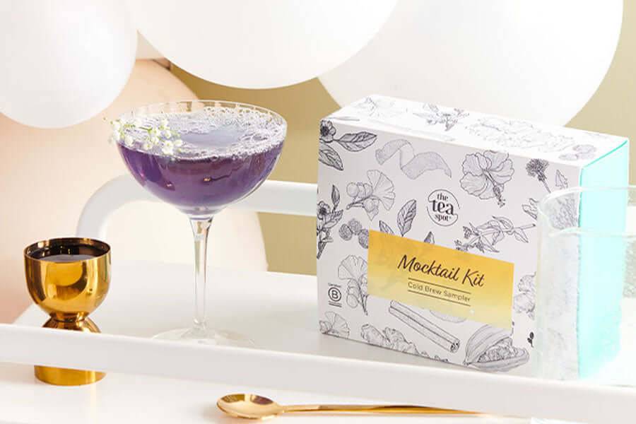 a purple tea mocktail sits on a bar cart next to a box reading mocktail kit