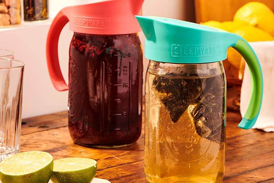 two mason jars with tea bags and tea in them sit on a table with craft cold brew filters attached