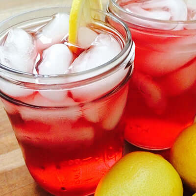two mason jar cups of iced tea sit on a wooden surface next to two lemons