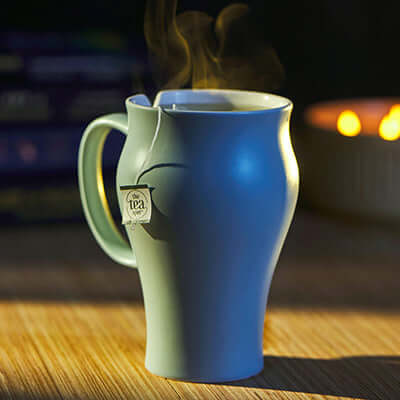 steamy mug of tea sits on a wooden surface with a candle burning in the background