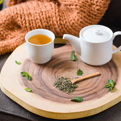 a teapot sits next to a cups of brewed tea on a wooden surface alongside peppermint leaves and a pile of tea