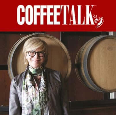 woman with glasses smiles and stands in front of aging barrels