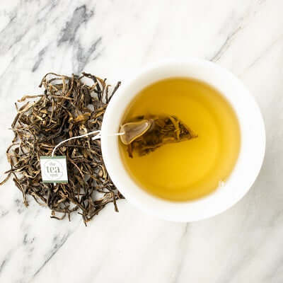 pu'er tea sachet brews in a white cup next to loose tea on a marble surface
