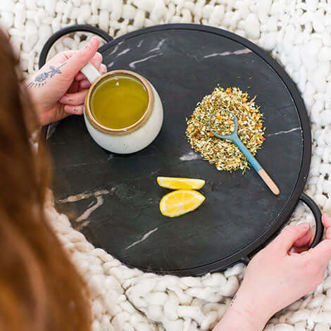a person sits over a tray with a cup of tea, lemons and a pile of loose tea