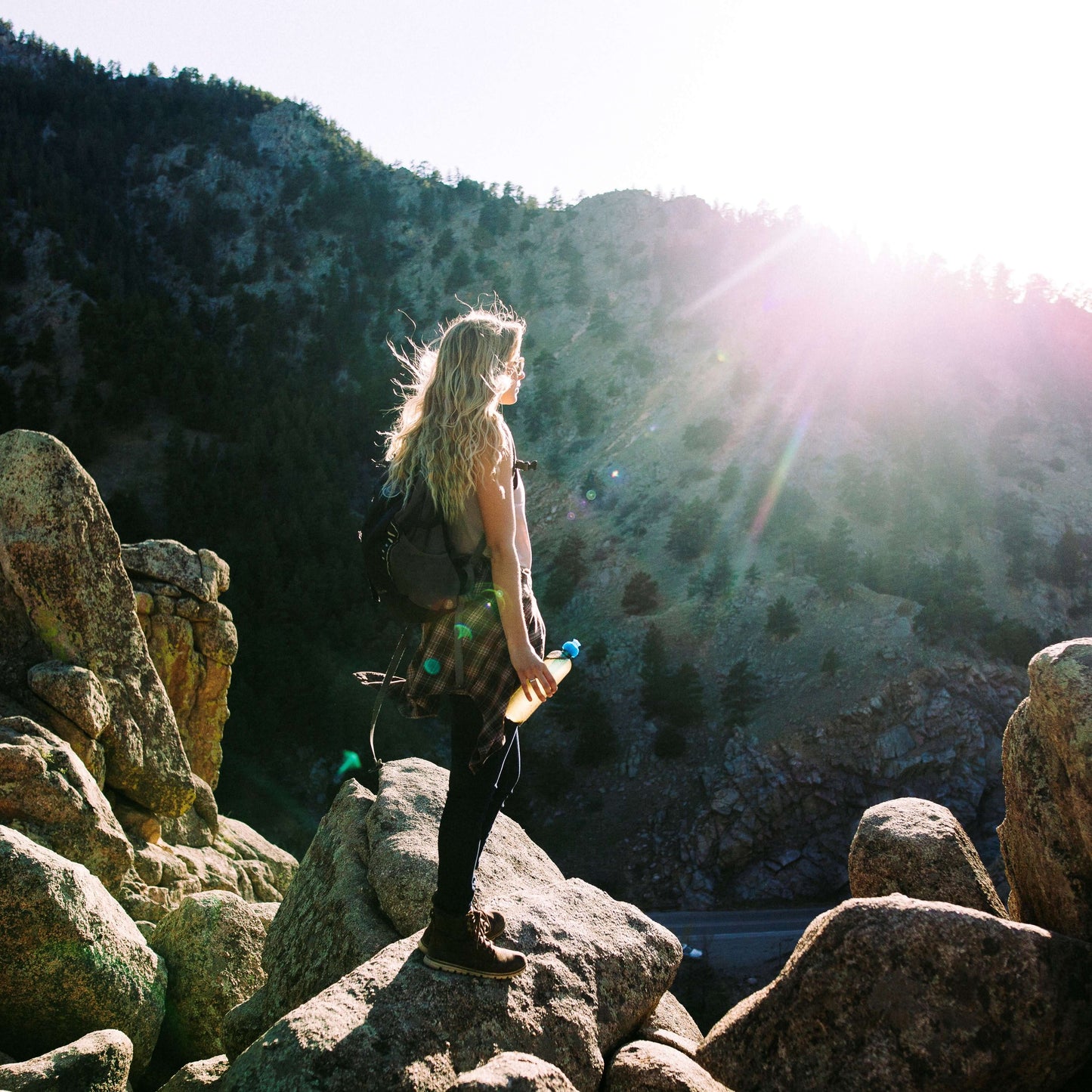 woman stands on rocks with a mountain background holding tea tumbler