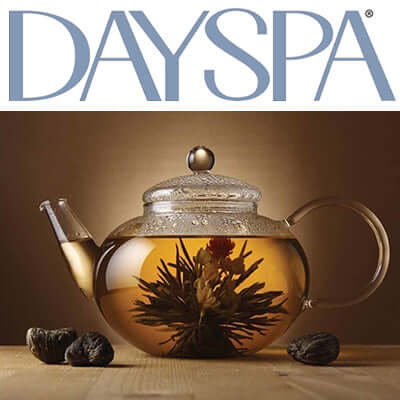 glass teapot with flowering tea brewed inside sits on a wooden surface beside small rocks