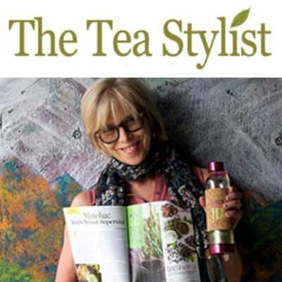 woman with glasses smiles and holds a book and tea tumbler