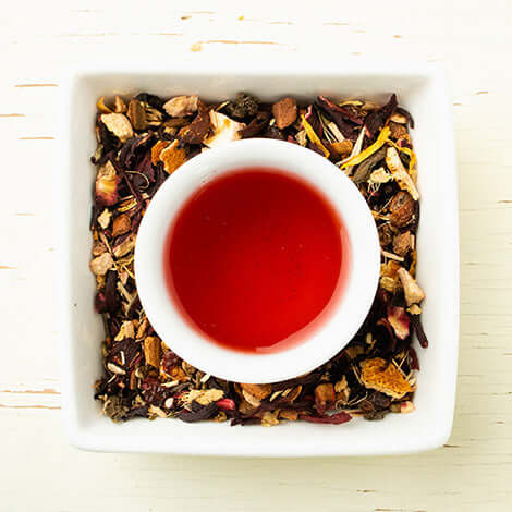 a brewed cup of tea sits in a dish of tea ingredients on a wooden surface