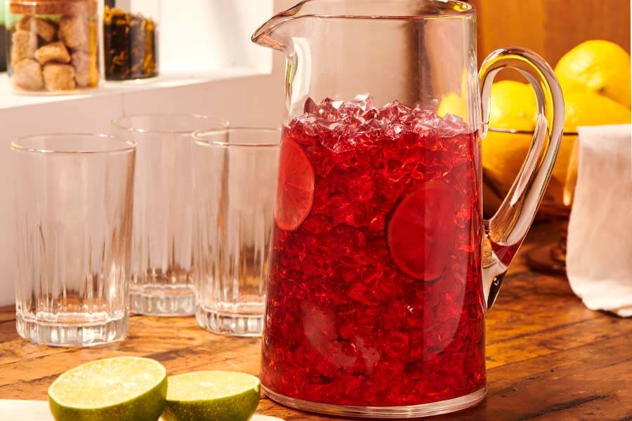 a pitcher of iced tea sits on a wooden countertop beside glasses and a sliced lime