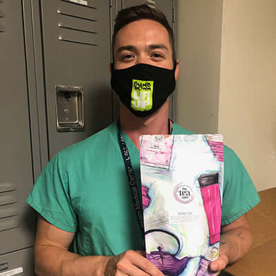 a nurse wearing a face mask and scrubs holds a bag of donated the tea spot tea