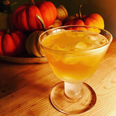 an herbal tea infusion cocktail sits on a wooden surface next to a plate of small pumpkins