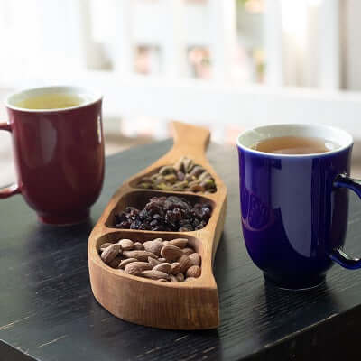 a black table with two cups of tea and a wooden dish of snacks