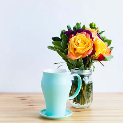 a blue teacup sits on a wooden table next to a vase of flowers