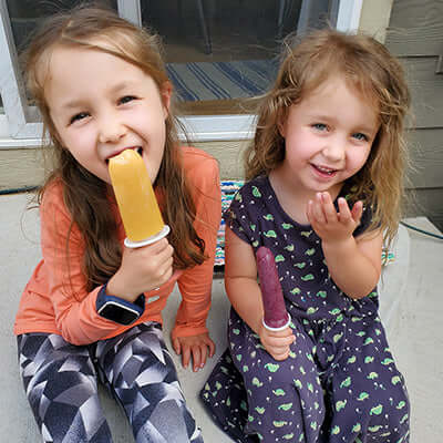 two children smile while they eat tea popsciles on porch steps