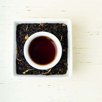 a white cup of brewed tea since in a white dish full of loose leaf tea blend on a wooden surface