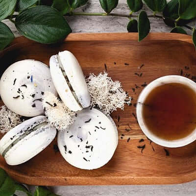 buttercream macaroons sit on a wooden dish next to a brewed cup of earl of grey tea