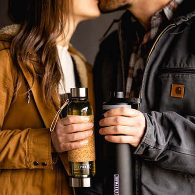 couple kiss as they hold tea tumblers in their hands