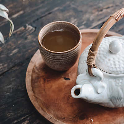 brewed cup of tea sits next to a teapot on a wooden table