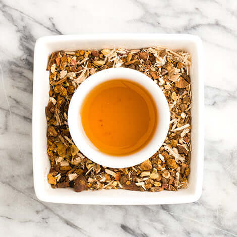 cup of brewed ashwagandha tea sits in a dish full of tea ingredients on a marble surface