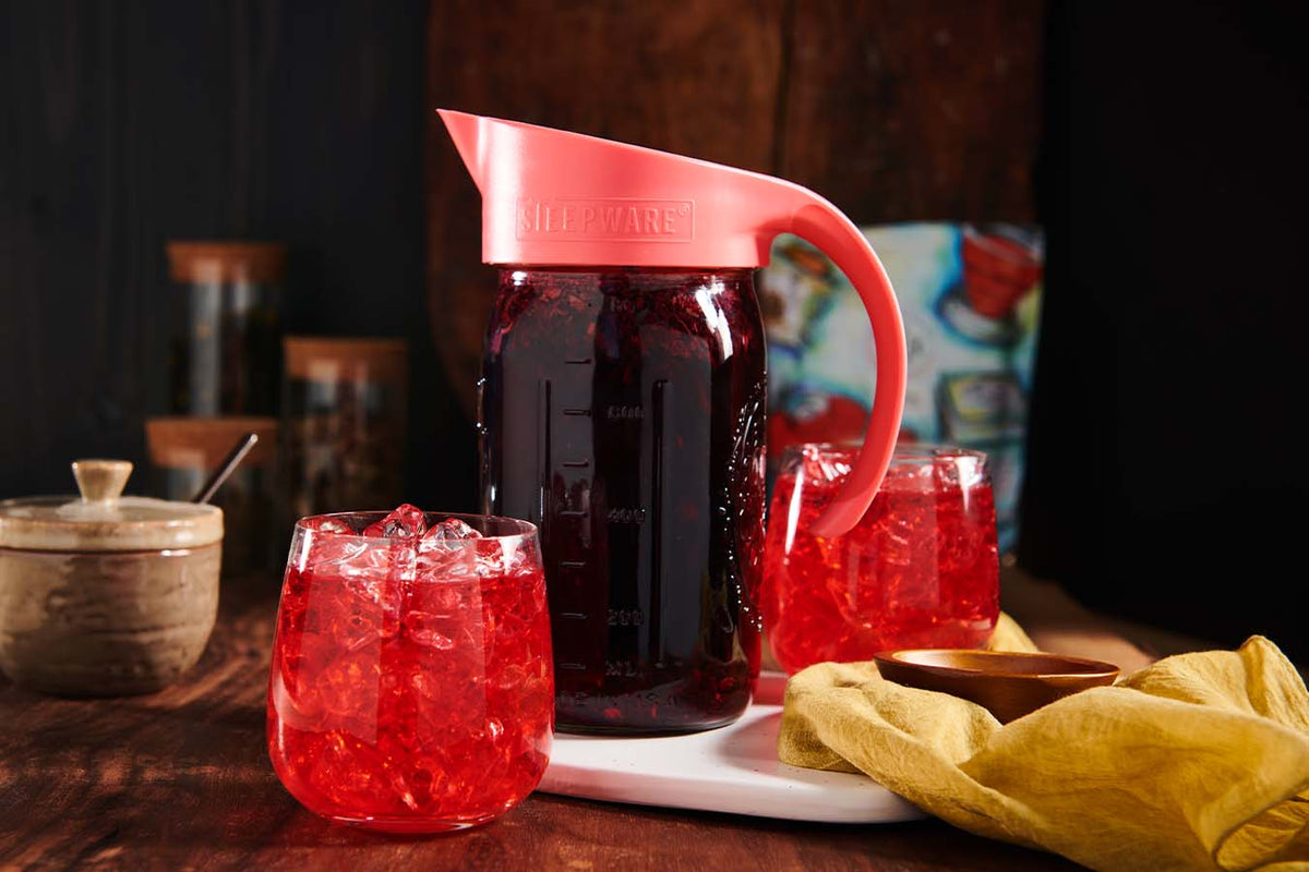 a filter lid sits atop a mason jar with cold brewed tea in it, surrounded by two glasses with cold brew tea in them 