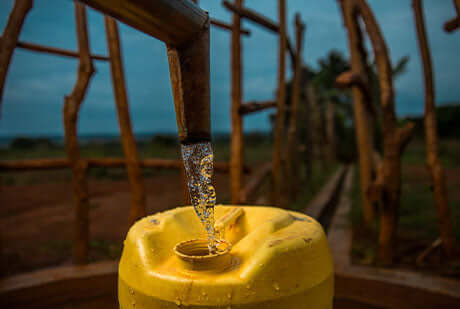 a pipe pours clean water into a yellow jug