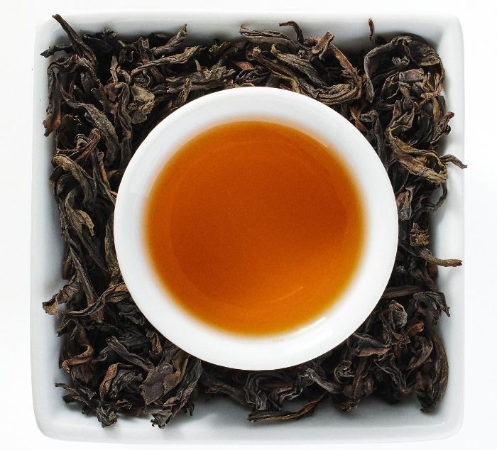 White cup of tea with da hong pao tea surrounded by dry tea leaves on a white background