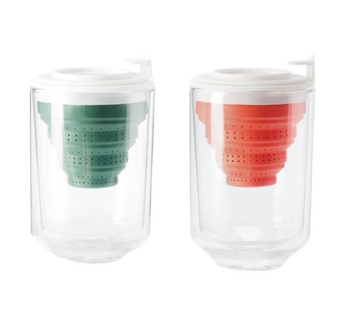 two double walled glass tea mugs sit next to each other. One with a green infuser and one with a pink. 