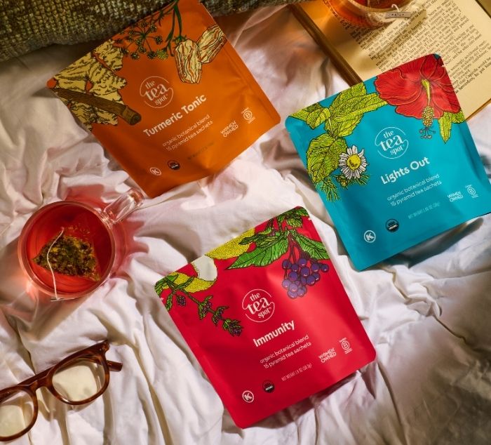 packages of evening teas sit on bed next to brewed cups of tea and book