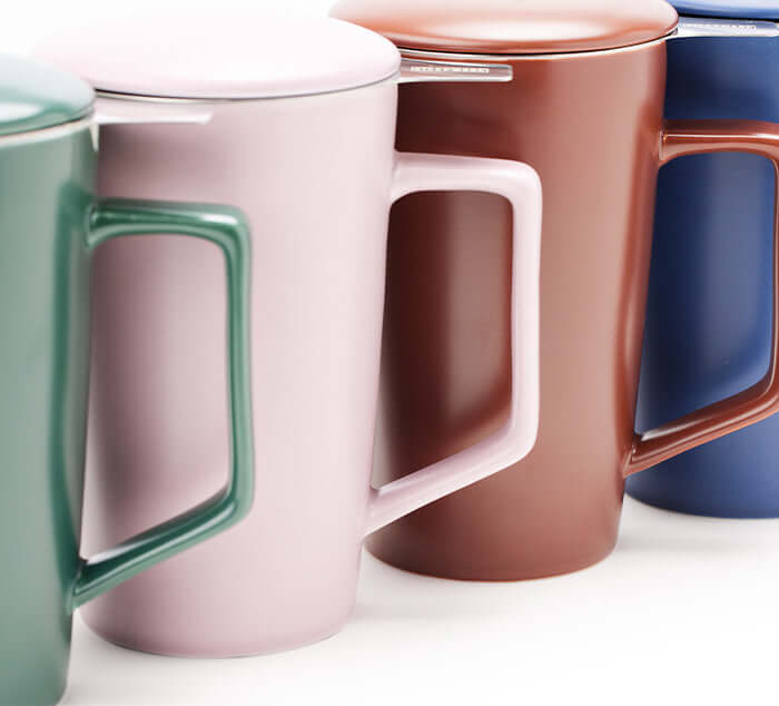 a set of four ceramic mugs, green, pink, brown, and blue in a line