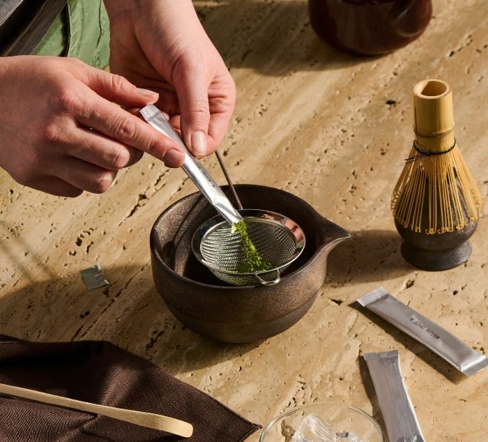 a person sifts matcha into a ceremonial matcha bowl