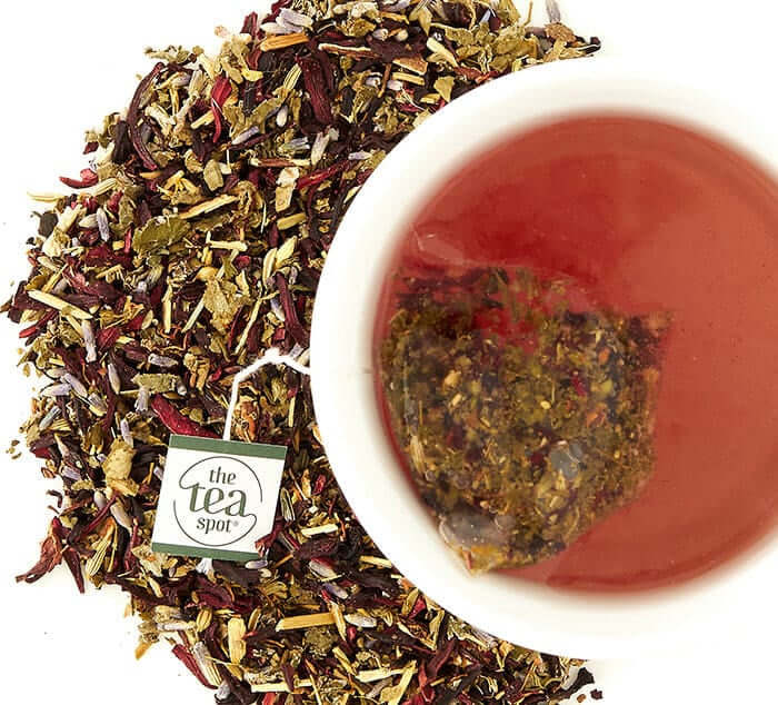 cramp comfort sachet brews in a white tea cup next to loose tea on a white background