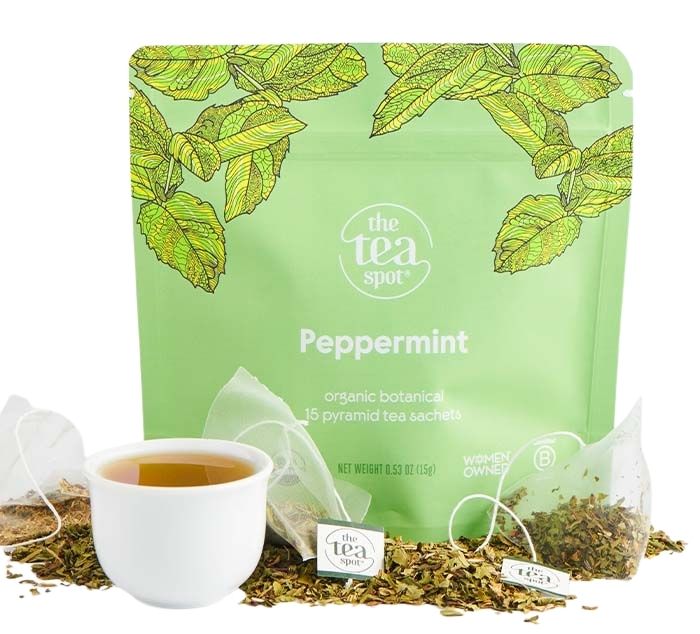 Tea package with peppermint flavor, cup of tea, and loose tea leaves on a white background