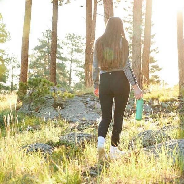 a girl walks in a forest holding a tea tumbler