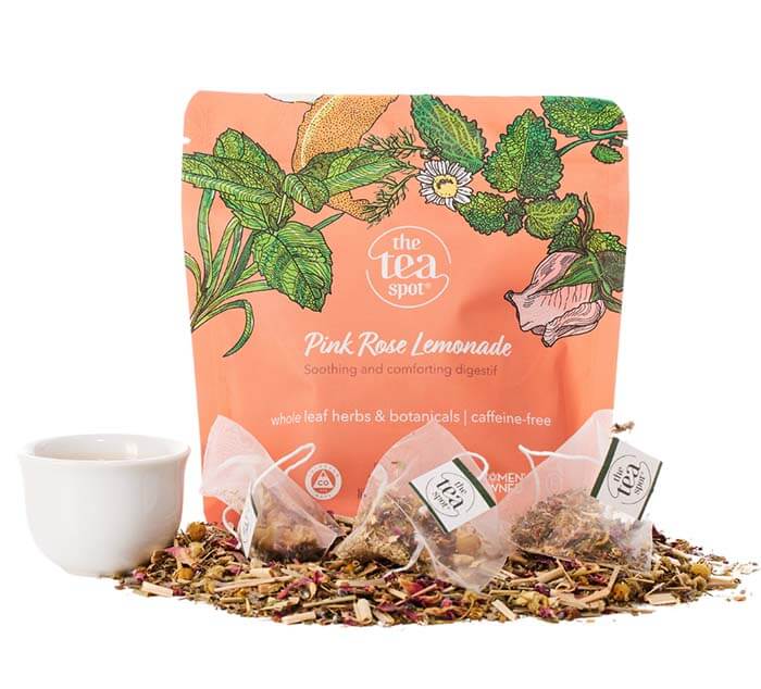 a bag reading pink rose lemonade sits behind tea bags and loose leaf tea and a tea cup