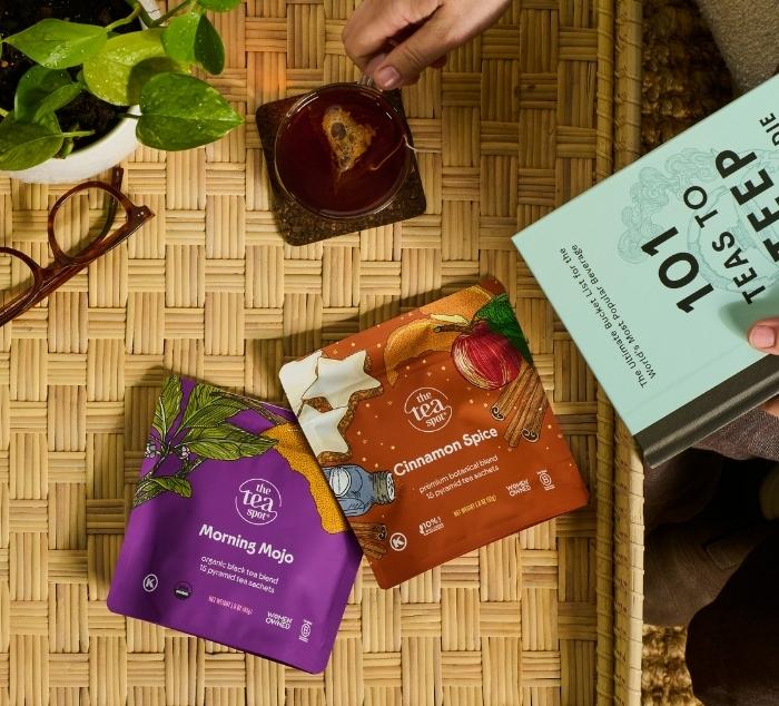 a person reaches for a mug of tea while holding a book titled 101 teas to steep before you die