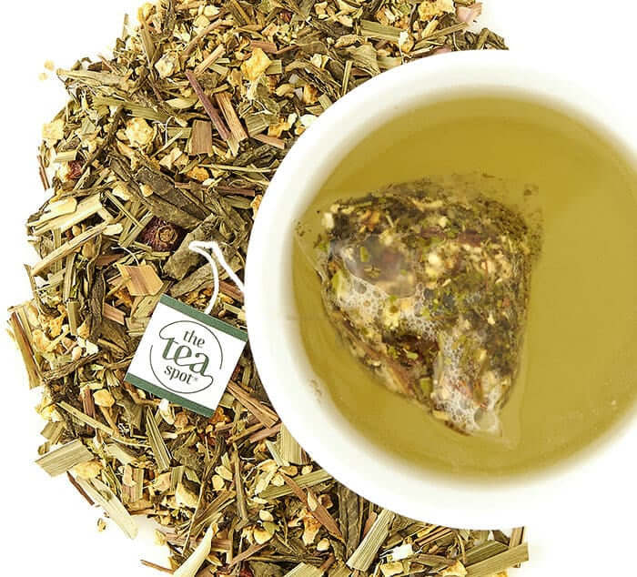 decaf lemon ginger green tea sachet brewing in a white teacup over a pile of loose tea
