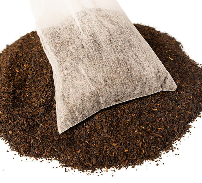 Nilgiri Black Iced Tea Pouch sits on a pile of black loose leaf tea